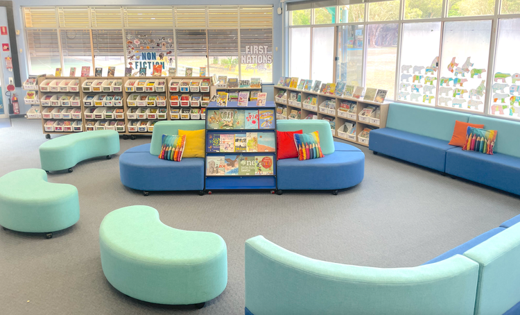Bright blue lounge and ottomans with bookshelves in the background and bright pillows