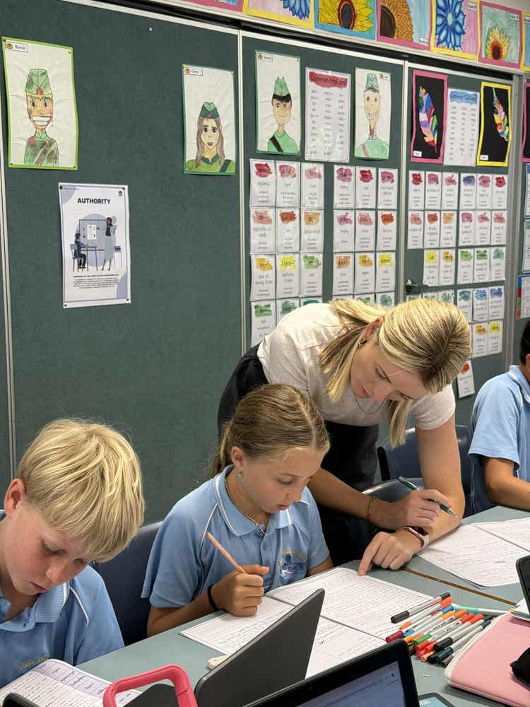 Teacher leaning down helping two students