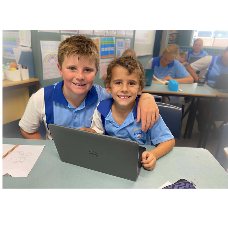 two students sitting in a classroom with a laptop