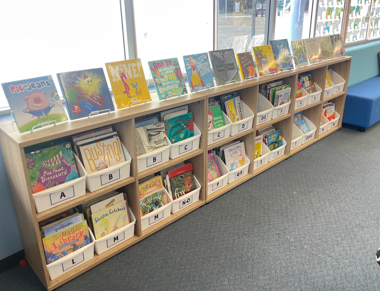 Junior fiction section with picture books held in white tubs organised in alphabetical order facing forward