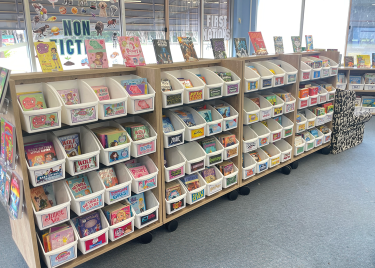 Senior fiction collections and series section of library with books in white tubs facing forward on book shelves