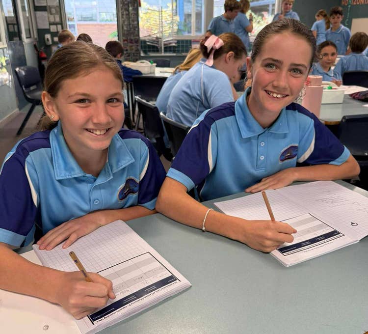 Two students sitting at their desk writing and smiling