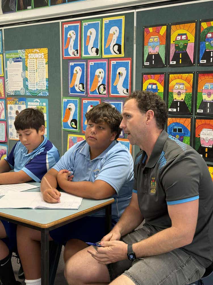 male teacher sitting with two students at desk